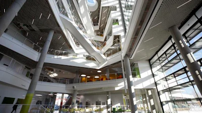 Modern spiral atrium with multiple levels, glass railings, natural skylighting, and concrete columns in contemporary building interior