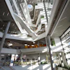 Modern spiral atrium with multiple levels, glass railings, natural skylighting, and concrete columns in contemporary building interior