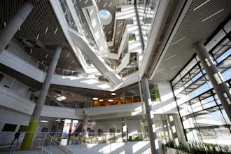 Modern spiral atrium with multiple levels, glass railings, natural skylighting, and concrete columns in contemporary building interior