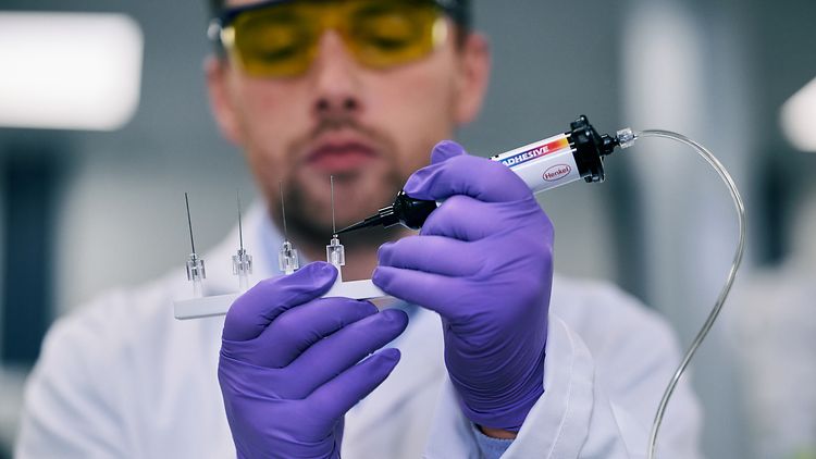 Scientist in yellow-tinted glasses and purple gloves handling laboratory equipment and syringe in clinical setting