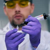 Scientist in yellow-tinted glasses and purple gloves handling laboratory equipment and syringe in clinical setting