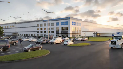 Modern industrial warehouse facility with blue and white facade, parking lot with vehicles, and landscaped grounds at dusk