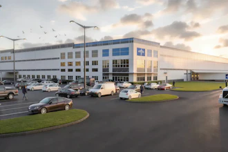 Modern industrial warehouse facility with blue and white facade, parking lot with vehicles, and landscaped grounds at dusk