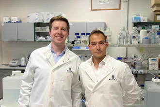 Two scientists in white lab coats smiling in a modern laboratory with equipment and supplies in the background