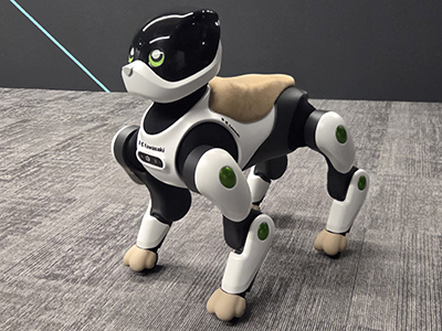Black and white robotic quadruped dog with tan accents and green eye lights standing on gray carpet