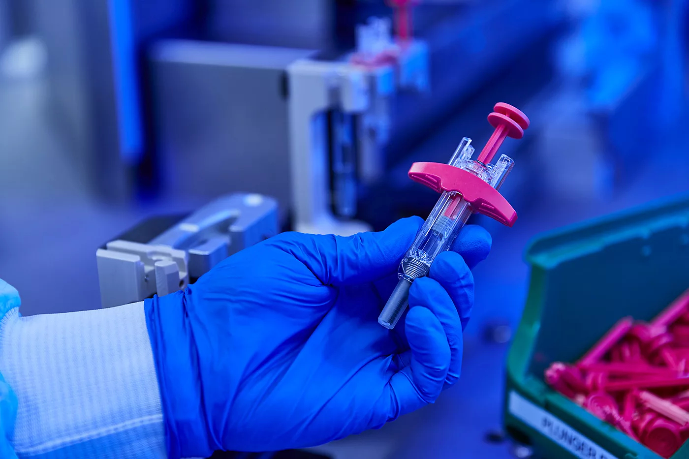 Gloved hand holding a syringe with pink plunger in laboratory setting