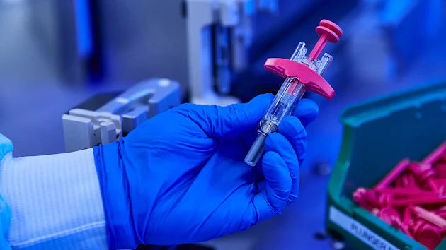 Gloved hand holding a syringe with pink plunger in laboratory setting