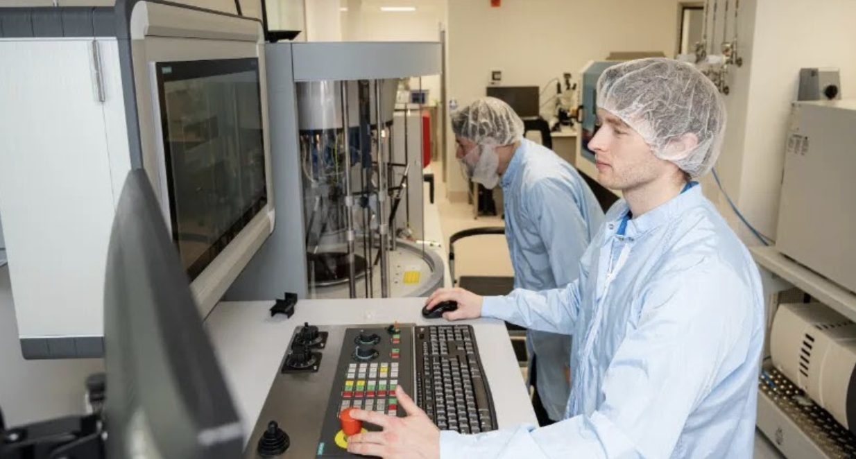 Two laboratory technicians in hairnets operating advanced analytical equipment in a clinical facility.