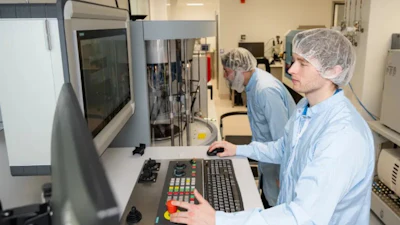 Two laboratory technicians in hairnets operating advanced analytical equipment in a clinical facility.