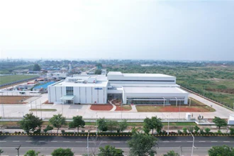 Aerial view of modern industrial manufacturing facility with white buildings, landscaped grounds, and surrounding agricultural landscape