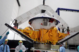 Spacecraft module with golden thermal blankets suspended in assembly facility with technicians and overhead support structure